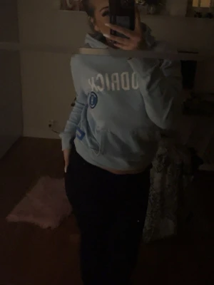 Hoodrich Ljusblå hoodie  - Säljer en ljusblå hoodie från hoodrich med vit text på bröstet och en rund logga på sidan. Hoodien har en klassisk huva och magficka, samt ribbade muddar vid ärmslut och nederkant. Perfekt för en avslappnad och sportig stil.