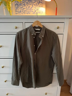 Olivgrön skjorta från Samsøe Samsøe - Snygg olivgrön skjorta från Samsøe Samsøe i bomull. Skjortan har klassisk krage med knappar, lång ärm och regular fit. Perfekt till jeans eller chinos för en clean och stilren look.