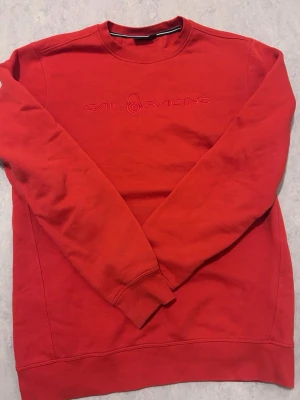 Röd sweatshirt från Sail Racing - Röd sweatshirt från Sail Racing med broderad logga framtill. Klassisk rund halsringning och långa ärmar. Tillverkad i mjuk bomull för en bekväm känsla. Perfekt för en avslappnad och stilren look.