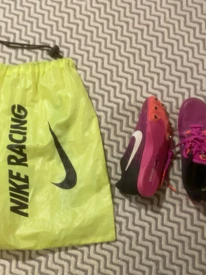 Nike Racing löparspikes rosa - Riktigt sköna skor enligt min galna friidrotts galna dotter. Säljer ett par Nike Racing löparspikes i rosa med svart och vitt. Skorna har metallspikar under sulan för extra grepp på löparbanan. Medföljer en gul Nike Racing-påse med snörstängning. Perfekta för friidrott och tävling.