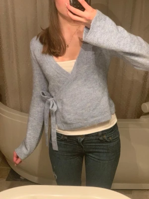 Ljusblå omlottkofta - Jättefin ljusblå omlottkofta med långa ärmar och knytband i sidan. Koftan har en mjuk, stickad känsla och en avslappnad passform. Säljer den då den inte längre kommer till användning, kontakta mig om ni undrar något💗