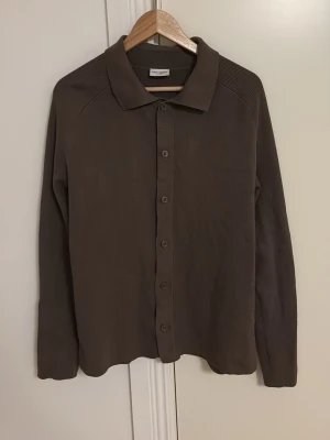 Brun ribbad skjorta/overshirt John Henric - Snygg brun skjorta/overshirt från John Henric i ribbat material. Skjortan har klassisk krage, långa ärmar och knäppning framtill med matchande knappar. Perfekt för en stilren och enkel look.