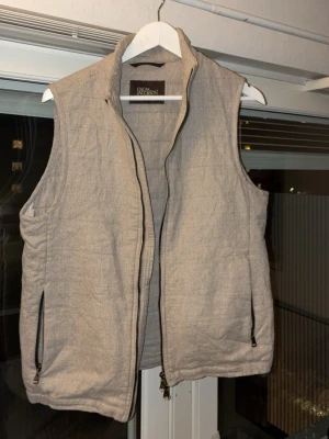 Beige quiltad väst från Oscar Jacobson - Stilren beige linneväst från Oscar Jacobson med dragkedja framtill. Västen har två fickor med dragkedja, samt en innerficka,  och en clean look som passar till många våren.                                       Nypris ligger på 3000kr, mitt pris är 1400kr