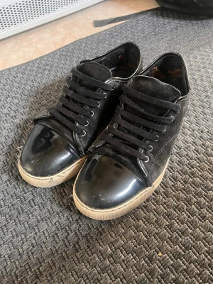 Svarta Lanvin sneakers cap toe - DUSTBAG MEDKOMMER! Snygga svarta sneakers från Lanvin med klassisk låg profil. Skorna har ovandel i mocka och tåparti i blankt lack, samt vita gummisulor. Svarta skosnören och diskret logga på sulan. Perfekta för dig som gillar stilrena och exklusiva sneakers. Ganska slitna mest invändigt men lite längst ut på ena skon också. Men inget som märks när dom används! Nypris: 5000kr Mitt pris: 899 Storlek 43 men passar större också! Skriv vid minsta lilla så svarar jag direkt!✌️