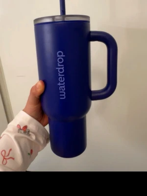 Blå Waterdrop mugg med sugrör - Stor blå mugg från Waterdrop med handtag och sugrör. Rymmer 1100 ml och har en stilren, cylindrisk form. Tillverkad i tåligt plastmaterial och perfekt för att hålla drycken kall eller varm under dagen.