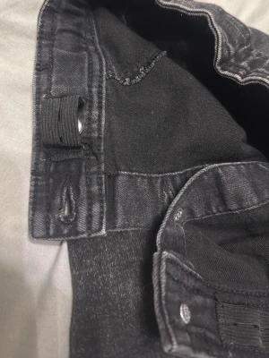 Svart jeanskjol med hög midja st. 146 - Säljer en svart kort jeanskjol med hög midja och synliga sömmar. Kjolen har en klassisk femficksdesign och knappstängning i midjan. Perfekt till sneakers eller boots för en cool vardagslook. Storlek 146.