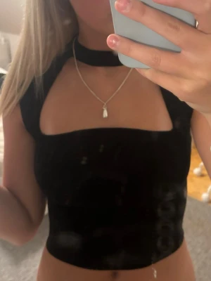 Svart croppad zara topp - Trendig svart croppad topp med unik choker-detalj runt halsen och breda axelband. Toppen har en tight passform och är perfekt för att skapa en edgy look. Materialet känns mjukt och stretchigt, vilket gör den bekväm att bära. Köpt på zara, storlek s men liten i storlek 