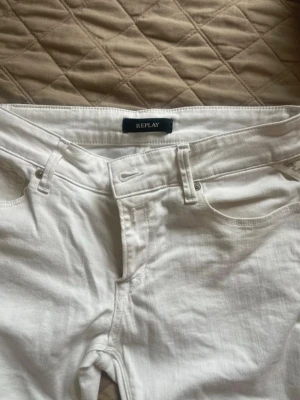 Vita lågmidjade jeans  - Säljer ett par vita jeans från Replay med bootcut-modell och klassisk femficksdesign. Jeansen har normal midja och är tillverkade i ett mjukt denimtyg som sitter snyggt. Perfekta för dig som vill ha en clean och fräsch look. Midjemått 34 innebenslängd 69cm