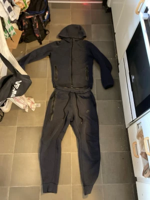Mörkblå hoodie från Nike med dragkedja - Säljer en mörkblå hoodie från Nike med dragkedja framtill och två fickor med dragkedja. Hoodien har en klassisk huva och ribbade muddar vid ärmslut och nederkant. Perfekt för chill dagar eller träning. Materialet känns mjukt och bekvämt.