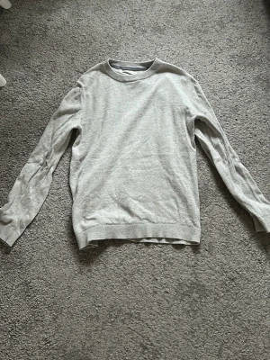 Ljusgrå stickad tröja från MNG - En stilren ljusgrå stickad tröja från Arket med rund halsringning och långa ärmar. Tröjan har ribbade muddar vid ärmslut och nederkant. Perfekt basplagg i mjukt material som passar till det mesta.  Den är inte strykt, därför är den skrynklig. 
