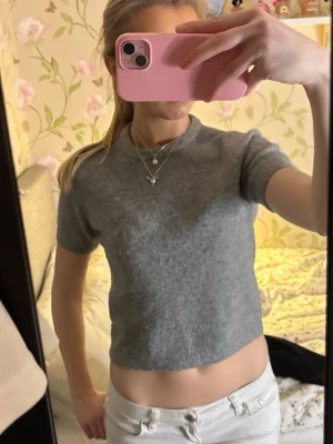 Grå croppad stickad topp - Säljer en enkel och stilren grå croppad stickad topp med korta ärmar och rund hals. Perfekt till jeans eller kjol för en chill look. Supermjuk och skön att bära.