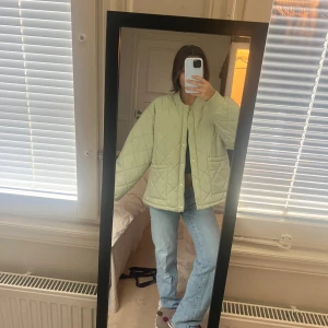 Ljusgrön quiltad pufferjacka - Säljer en ljusgrön pufferjacka med quiltat mönster och rund hals. Jackan har två stora fickor framtill, tryckknappar och en loose passform. I storlek S