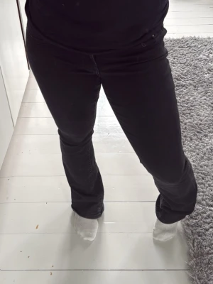 Svarta bootcut jeans - Säljer ett par svarta bootcut jeans med klassisk femficksdesign och silverfärgade detaljer på bakfickorna. Jeansen har en något utsvängd passform nedtill och är tillverkade i ett mjukt denimtyg som sitter snyggt på kroppen. Superfina byxor men tyvärr för stora för mig.