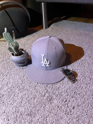 Grå LA keps från New Era - Tjena, säljer denna gråa keps från new era med LA tryck eftersom den inte längre passar mig. Kepsen är i princip aldrig använd i 9/10 skick. Kepsen är storlek 57,7. (PRISET ÄR INTE FAST)