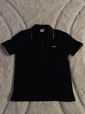 Svart pikétröja från BOSS - oanvänd boss piké tröja. storlek: 14 S. nypris: 800kr. Mitt pris: 450. hör av dej vid intresse! 