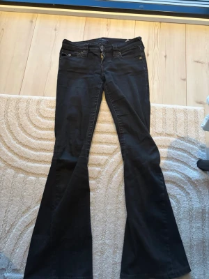 Svarta flare jeans från True Religion - Säljer ett par svarta True Religion Joey Low Rise Flare jeans. De har låg midja, utsvängda ben och detaljer som synliga sömmar och fickor fram och bak.