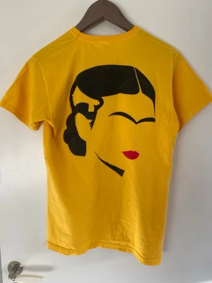 Frida Kahlo T-shirt - Gul T-shirt med Frida Kahlo tryck över ryggpartiet.