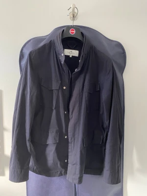 John Henric field jacka strl S (passar även M) - Säljer en field jacka/overshirt ifrån John Henric i bomull. Jackan är i fint skick utan defekter. Perfekt till vardags under alla väderförhållanden. En regnluva går att väckla ut i kragen med en dragkedja (se sista bilden). Funkar som ytterlager med en väst under när vädret är kallare. Finns dragkedja och knappar för att stänga. Storlek S men passar även M ~175-185 cm skulle jag rekommendera. Jackan kostade ~ 2000 kr ny, men säljs inte längre i denna modell. Hör av er vid frågor och funderingar!