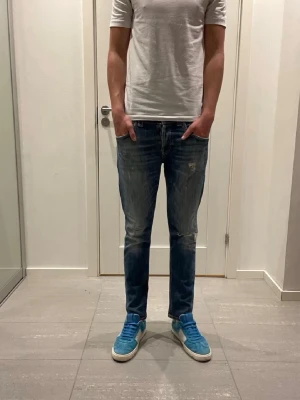 Blå slitna jeans från Dondup - Säljer ett par blå jeans från domdup med snyggt sliten tvätt och diskreta slitningar på låret. Jeansen har rak passform och klassisk femficksdesign. Perfekta för en avslappnad och trendig look.