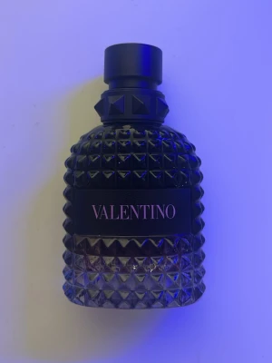 Valentino Uomo Born In Roma Intense - Valentino Uomo Born In Roma Intense Eau de Parfum med en elegant svart glasflaska dekorerad med nitar och ett stilrent svart lock. Flaskan har en lyxig, mönstrad yta och kommer i en svart kartong med rosa detaljer. Köpt på kicks för 1000kr. Det är ca 45/50ml kvar. 
