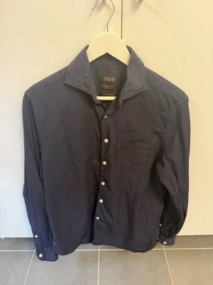 Mörkblå skjorta från Oscar Jacobson, stl S - Snygg mörkblå skjorta från Oscar Jacobson i bomullstwill. Klassisk modell med bröstficka, vita knappar och lång ärm. Perfekt för dig som gillar stilrena och tidlösa plagg. Regular fit och mjukt material för skön känsla.