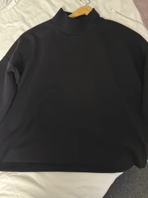 Svart tre kvarts ärmad tshirt från Carin Wester - Säljer en svart polotopp från Carin Wester. Toppen har en hög krage och trekvarts ärm, perfekt för lager på lager. Enkel och stilren design som passar till det mesta. Materialet känns mjukt och bekvämt.