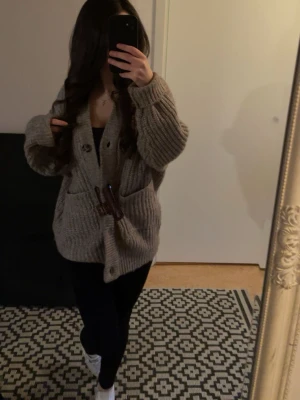 Beige stickad kofta med träknappar - Mysig beige stickad kofta med grov ribbstickning och stora träknappar. Koftan har två framfickor och en avslappnad, oversized passform. Perfekt för lager på lager och en chill look. Mysig och varm passar till både leggings och jeans