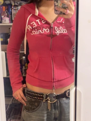 vintage Rosa hoodie från Hollister - Säljer en rosa zip-hoodie från Hollister med vit text på bröstet och huva med vita snören. Hoodien har fickor framtill och en figurnära passform. Köpt på en vintage store (där dom säljer märkeskläder)  i Seoul. 