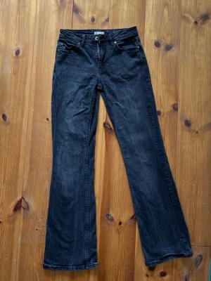 Svarta bootcut jeans med låg midja - Snygga svarta bootcut jeans med låg midja och klassiska fem fickor. Jeansen har en lätt tvättad look och raka ben som blir vidare nedtill. Perfekta för en avslappnad och trendig stil. Storleken är XS/32 och märket är från  Cubus