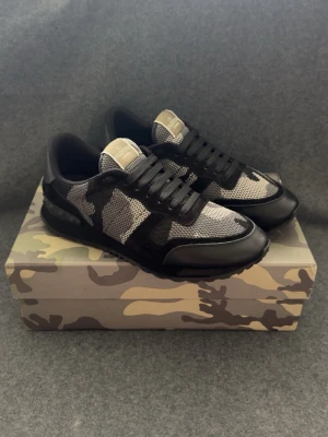 Svarta camo Rockrunners med nitar - Snygga Rockrunners i svart och grått camomönster med coola nitar på hälen. Skorna har en mix av mesh och mocka samt svarta skosnören. Sulan är svart och ger en sportig vibe. Perfekta för dig som gillar streetstyle och vill sticka ut.
