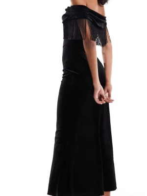 Svart sammetsklänning med fransar - Elegant svart långklänning i sammet med offshoulder-design och långa fransar längs överdelen. Klänningen har en figurnära passform och ger en lyxig känsla med sin mjuka yta och trendiga detaljer. Perfekt för dig som vill sticka ut med en unik look.