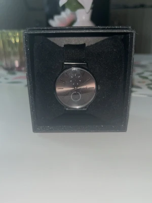 Svart klocka från Regal - Stilren svart klocka från Regal med rund urtavla och mesharmband i metall. Klockan har minimalistisk design med diskreta markeringar och en extra liten urtavla. Kommer i original ask, perfekt för dig som gillar enkel och modern stil. Den har en liten defekt se sista bild 