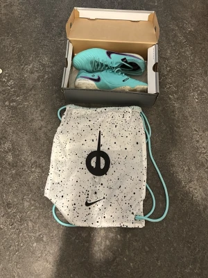 Nike Legend 10 Elite FG fotbollsskor - Säljer ett par Nike Legend 10 Elite FG fotbollsskor i en fräsch turkos färg med vita och lila detaljer. Skorna har låg profil och är tillverkade i syntetmaterial för bästa känsla på planen. Medföljer en vit och svart Nike-påse.