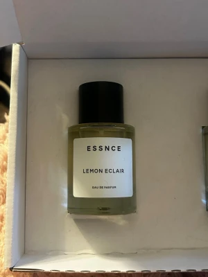 ESSNCE Lemon Eclair Eau de Parfum - Fräsch parfym från ESSNCE med doft av Lemon Eclair. Flaskan är rund och genomskinlig med svart lock och vit etikett. Perfekt för dig som gillar citrusdofter och stilren design. Endast testad