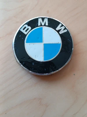 BMW emblem till bil - BMW emblem i plast och metall med klassisk svart, vit och blå design. Passar till bil och har texten 'BMW' på framsidan. Baksidan är svart och märkt med 'Made in Germany' samt artikelnummer. Perfekt för dig som vill byta ut ditt nuvarande emblem eller du kan ha den. 