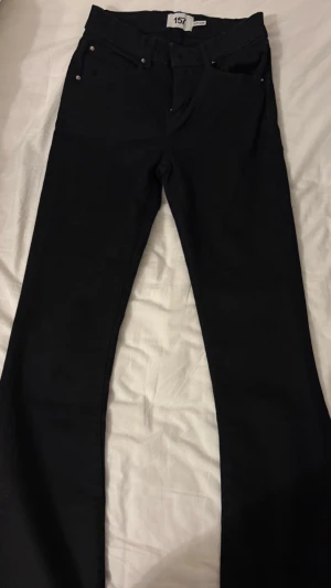 Svarta bootcut jeans - Säljer ett par svarta bootcut jeans med klassisk ficksmodell och normal midja. Jeansen har en stilren look och är perfekta för dig som gillar en tidlös och enkel stil. Materialet är denim med lite stretch för extra komfort.