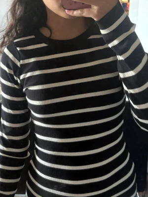 Svartvit randig ribbad långärmad topp - Säljer en svartvit långärmad topp med horisontella ränder och ribbad struktur. Toppen har en rund halsringning och sitter tight mot kroppen. Perfekt att styla med jeans eller kjol för en enkel men snygg look.