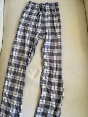 Rutiga pyjamasbyxor  - Mysiga pyjamasbyxor med gråvitt rutmönster och dragsko i midjan. Väldigt sköna och perfekta för slappa dagar hemma. Långa ben och elastisk midja för extra komfort.