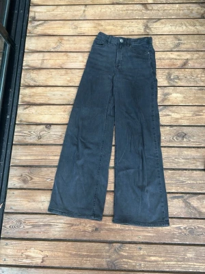Svarta vida jeans med hög midja - Säljer ett par svarta jeans med hög midja och raka, vida ben. Klassisk fyrficksmodel med knapp och dragkedja framtill. Jeansen har en avslappnad passform och är perfekta för en trendig och bekväm stil. Materialet är denim i bomull.