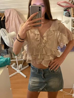 Volangblus Zara - Rosa beige blus i transparent material med vita broderade blommor och flera lager volanger. Blusen har v-ringning och korta ärmar med volangkant. Aldrig använd, hör av dig vid frågor eller intresse 💕 Jag är öppen för prisförslag