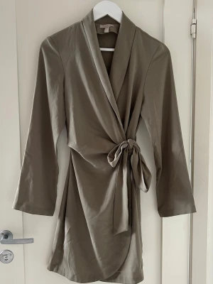 Klänning  - Khaki färgad klänning som går att knyta och justera själv, kommer med knappar inuti klänning. Storlek XS från H&M använd ett par gånger men hel och fin 