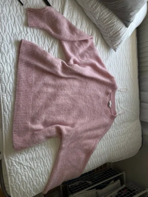 Ljusrosa  stickad tröja - Supermjuk stickad tröja i ljusrosa färg. Tröjan har en avslappnad passform, ribbade muddar vid ärmslut och nederkant samt rund halsringning. Perfekt för att hålla sig varm och snygg under kyliga dagar.