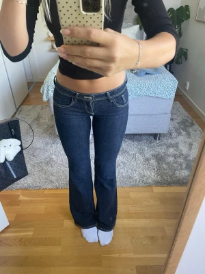 Mörkblå bootcut jeans med vita sömmar - Säljer ett par mörkblå bootcut jeans med vita kontrastsömmar och låg midja. Jeansen har klassiska fem fickor och är i ett stretchigt denimtyg som sitter snyggt på kroppen. Perfekta för dig som gillar en retro och trendig look.