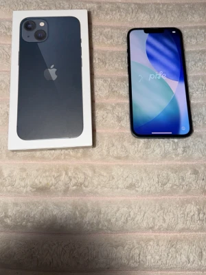 Mörkblå iPhone med dubbla kameror - Snygg mörkblå iPhone med stilren design och två bakre kameror. Telefonen har en stor skärm med tunna kanter och Apple-loggan på baksidan. Tillverkad i glas och metall för en premiumkänsla. Perfekt för dig som gillar modern teknik och snygg design, 128gb lagring.☺️