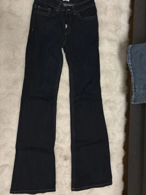 Mörkblå bootcut jeans med kontrastsömmar - Snygga mörkblå bootcut jeans med vita kontrastsömmar och dekorativa bakfickor med gul brodyr. Klassisk femficksmodell i denim med låg midja och utsvängda ben. Perfekta för en trendig och avslappnad look. Från nelly 