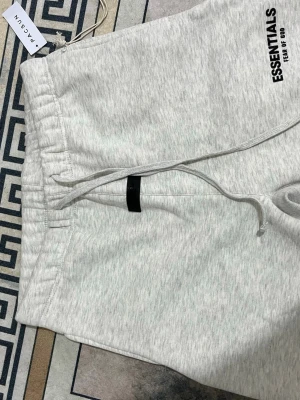 Grå mjukisbyxor Essentials - Ljusgrå mjukisbyxor från Essentials Fear of God med resår i midjan och dragsko. Byxorna har en avslappnad passform och är tillverkade i mjukt material. Perfekta för en chill och stilren look.