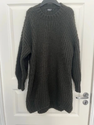 Mörkgrön stickad klänning från ONLY - Mysig oversized stickad klänning från ONLY i mörkgrönt. Tröjan har grovstickad struktur, rund halsringning och långa ärmar. Perfekt för lager på lager och chill höstoutfits.