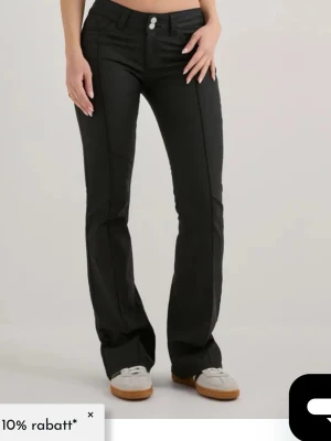 Svarta bootcut skinnbyxor med låg midja.  - Snygga svarta helt nya  skinnbyxor från Nelly  med bootcut passform och låg midja. Byxorna har två knappar framtill och raka ben som blir vidare nedtill. Perfekta för dig som gillar en clean och stilren look.