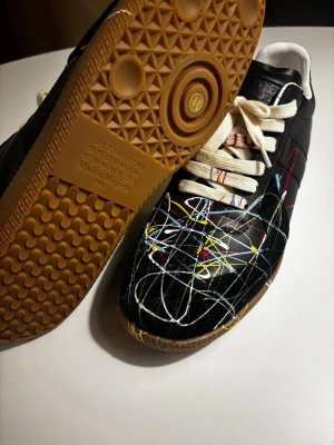 Maison Margiela paint splatter  - Maison Margiela sneakers i svart läder, skorna är för små för mig så vill gärna sälja snabbt så jag kan köpa nya. Skorna är 93ps. Pris kan dissekeras vid snabbare affär 