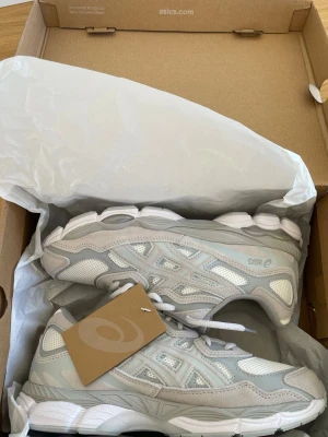 Asics Gel NYC  - Snygga sneakers från Asics nyc i cloud grey med meshpaneler och detaljer i syntet. Skorna har en chunky sula och klassisk snörning. Perfekta för dig som gillar sportig och clean stil.